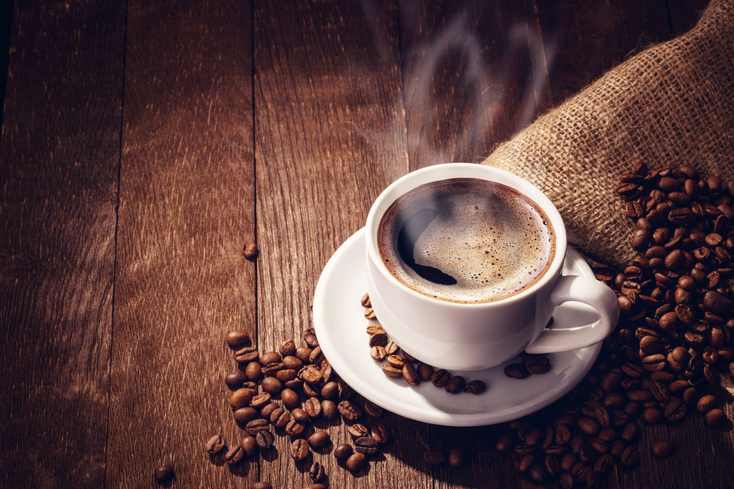 Steaming coffee cup on a wooden surface with coffee beans